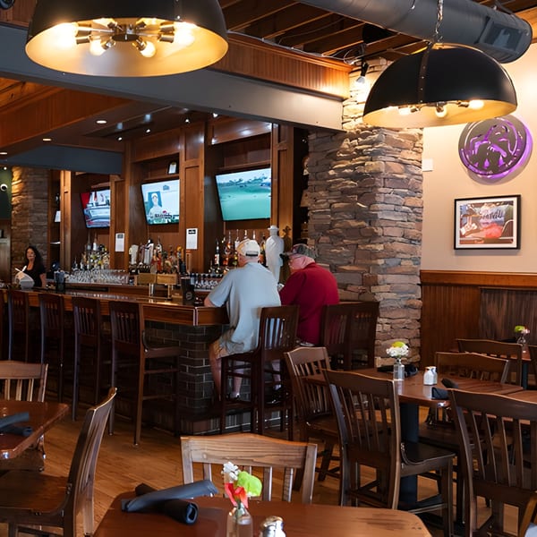 Two men sit at the Mayworth's Public House bar, with dining tables and stone pillars in the foreground.