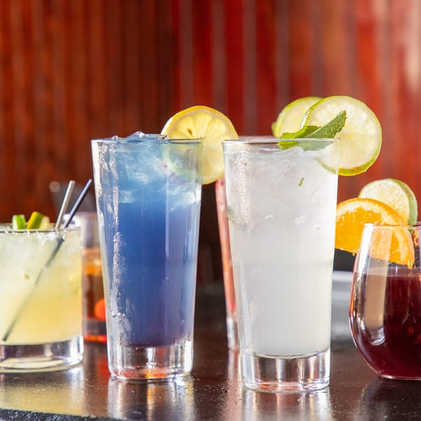 A variety of colorful cocktails, including blue, white, and red drinks, garnished with citrus and mint.