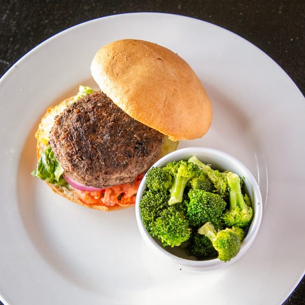 A Mayworth's Public House burger with lettuce, tomato, onion, and a side of steamed broccoli.