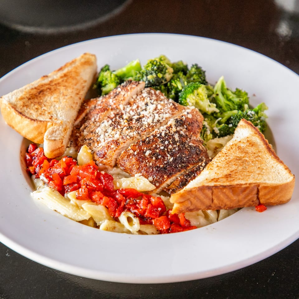 Grilled chicken with pasta, red peppers, broccoli, and toast on a white plate at Mayworth's.