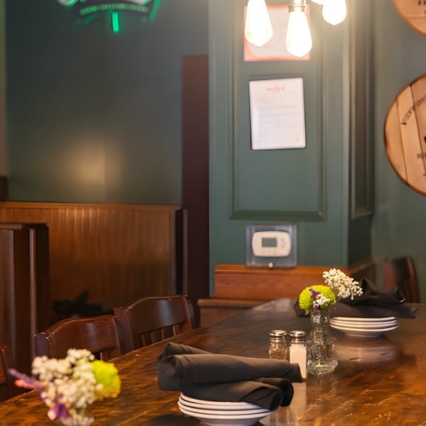 A long wooden table set with plates, napkins, salt and pepper shakers, and small flower arrangements.