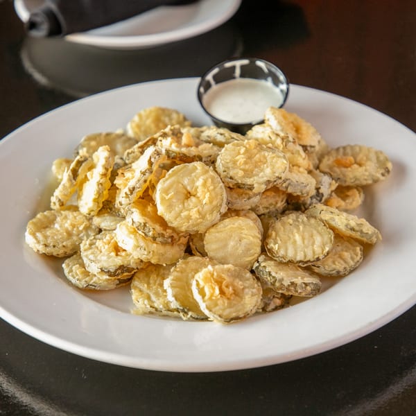 A white plate piled high with golden-brown fried pickles and a side of ranch dressing.